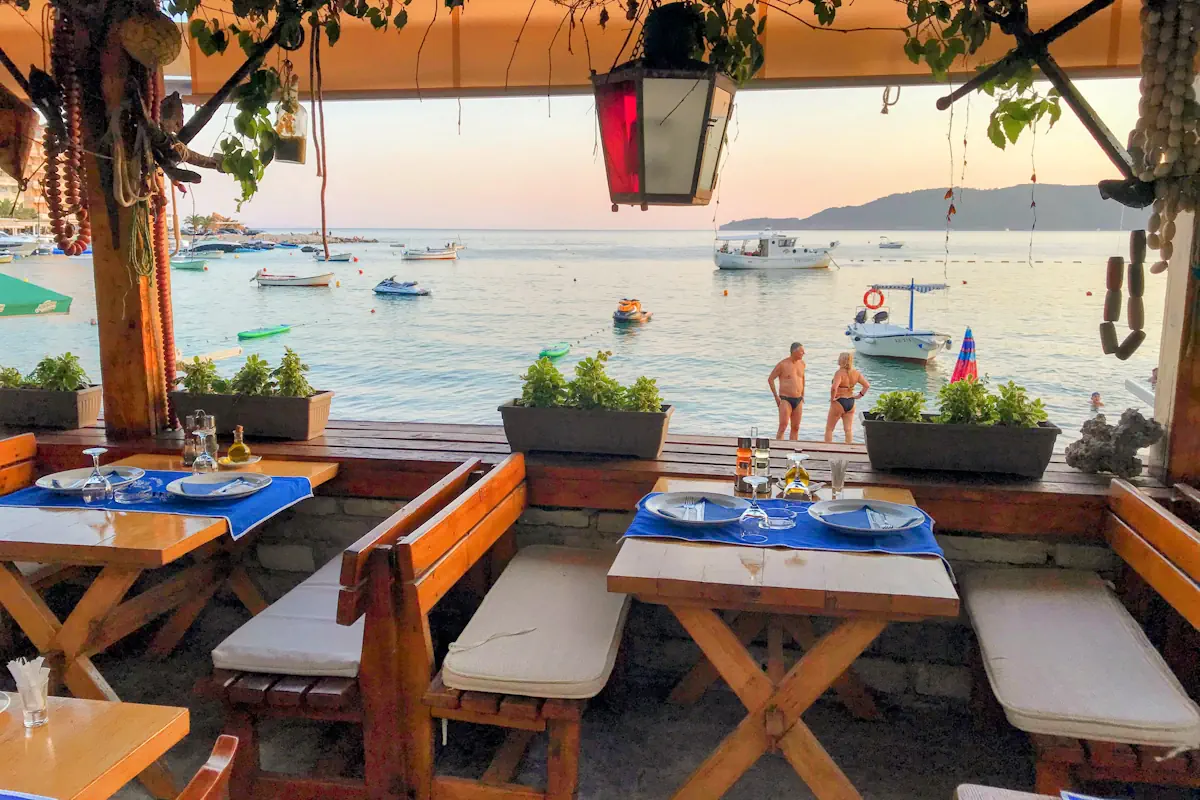 Waterfront tables at a traditional seafood tavern overlooking boats on the Adriatic Sea in Rafailovici