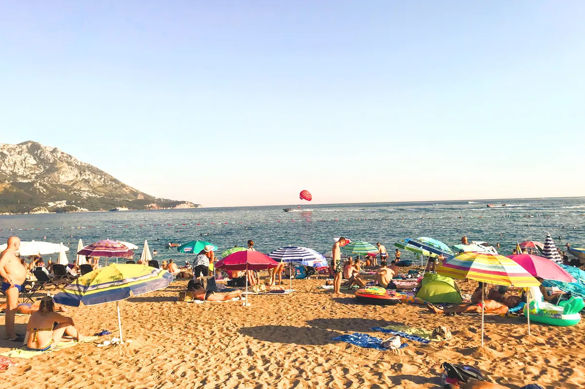 Bečići Beach near Budva, showing the wide sandy shoreline and a parasailer in the background