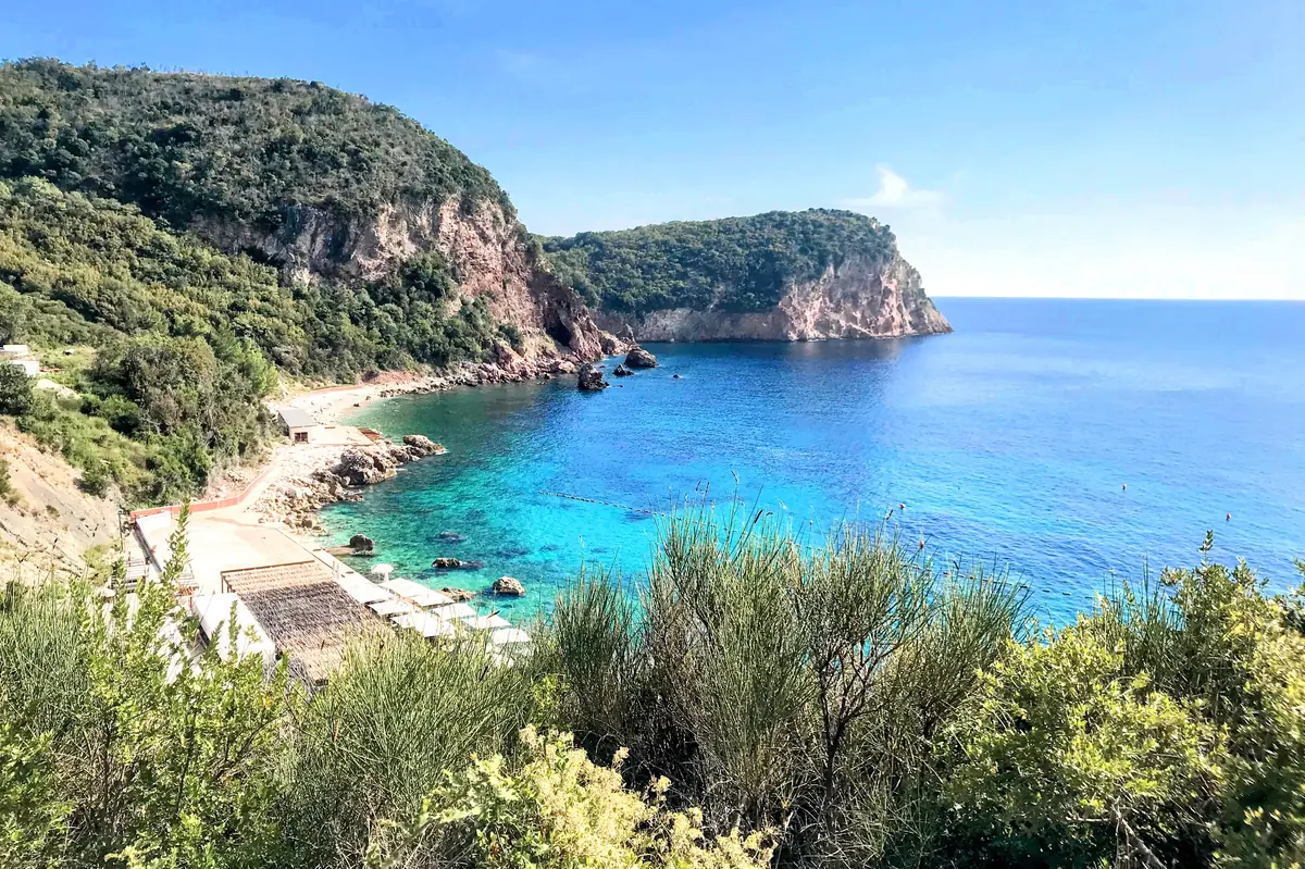 Galija Beach near Sveti Stefan, featuring a white beach bar wedged into dramatic red cliffs and clear turquoise water