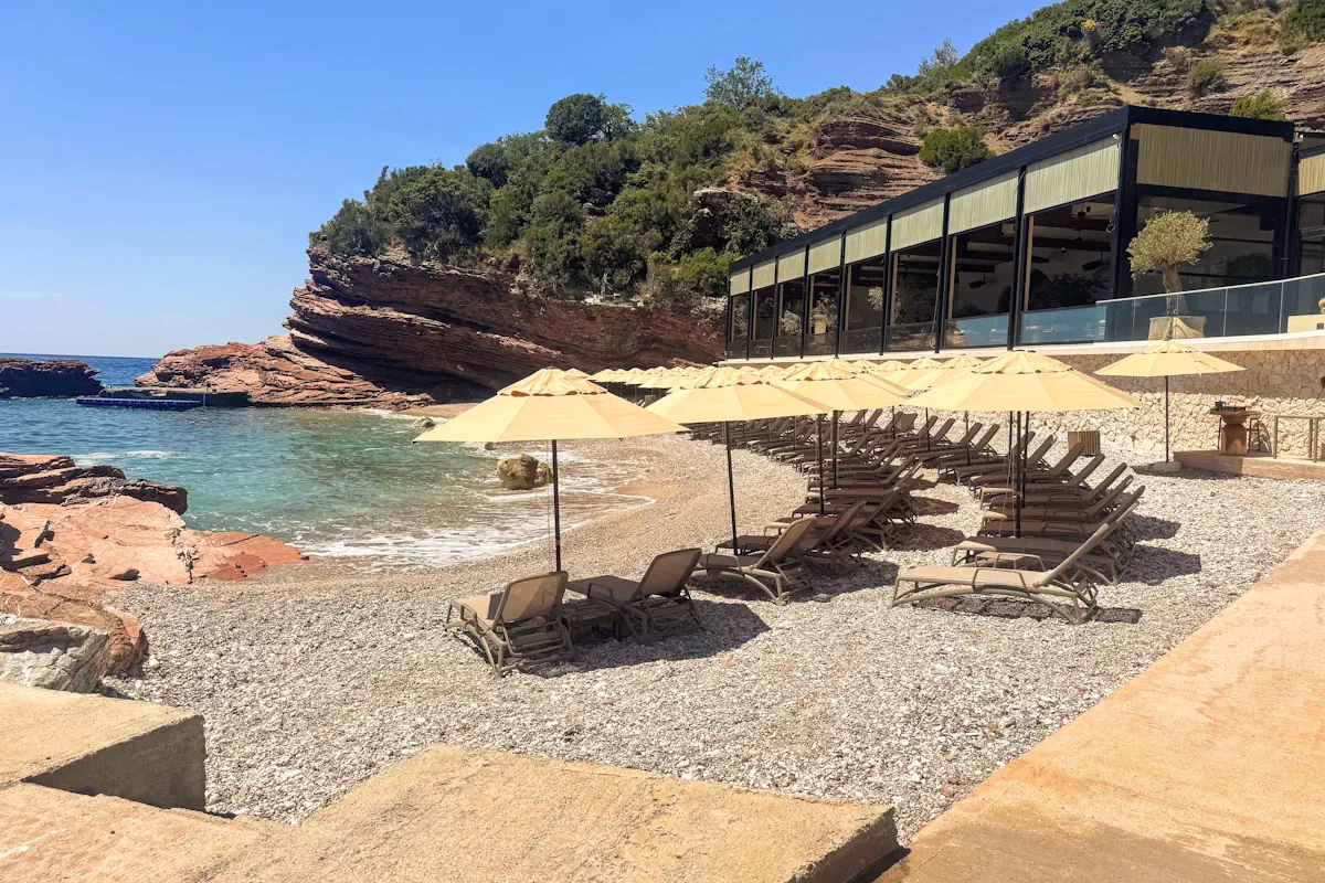 Close-up of the elegant sun loungers and beach club contrasting against the crystal-clear turquoise sea at Crvena Glavica, Sveti Stefan, Montenegro