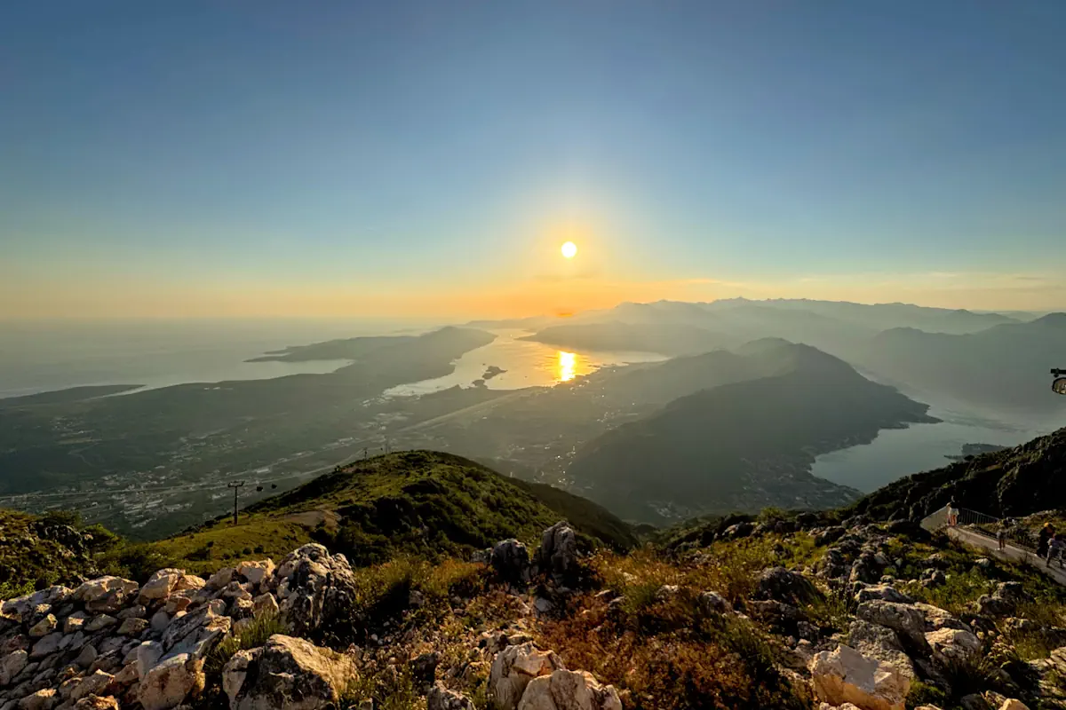 A cinematic high-altitude perspective from the Kuk station observation point looking out over the winding blue channels of Boka Bay as a vibrant golden hour sunset fills the sky with rich orange and amber tones