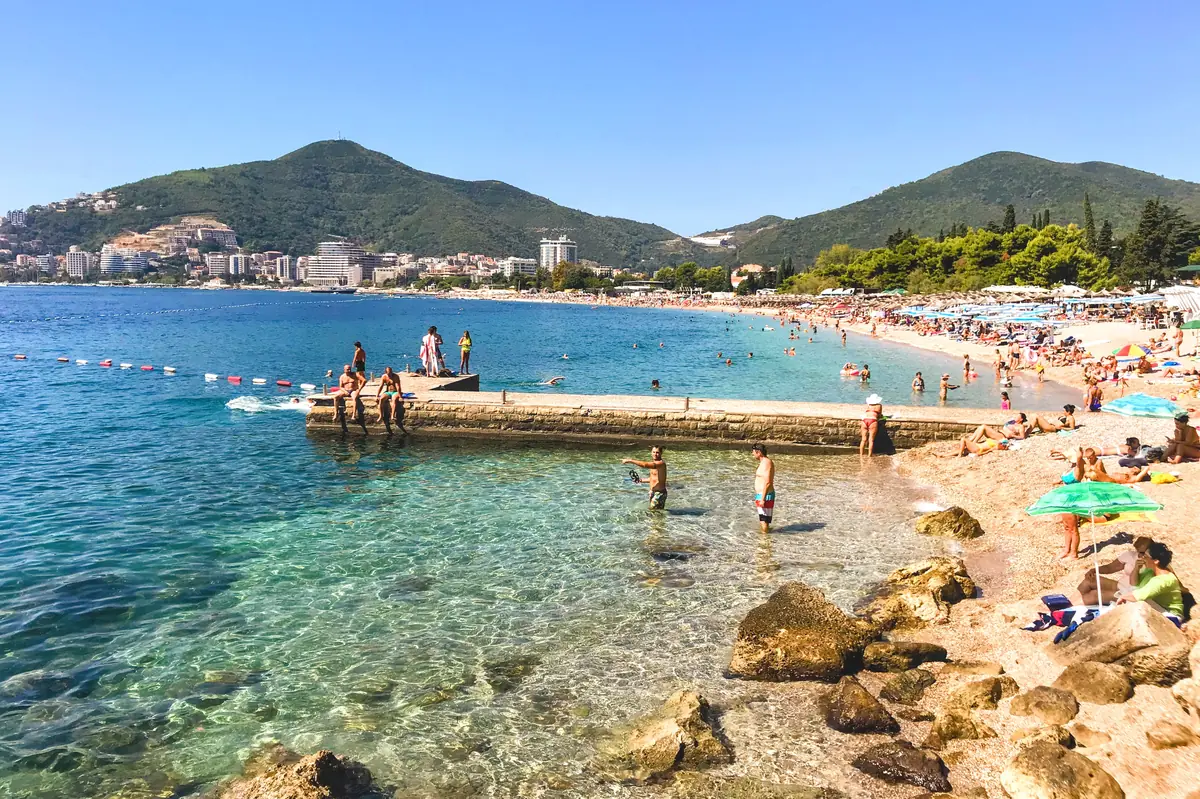 Slovenska Plaza with stone pier in Budva, the long main city beach with promenade and beach bars, Budva's townscape in the background