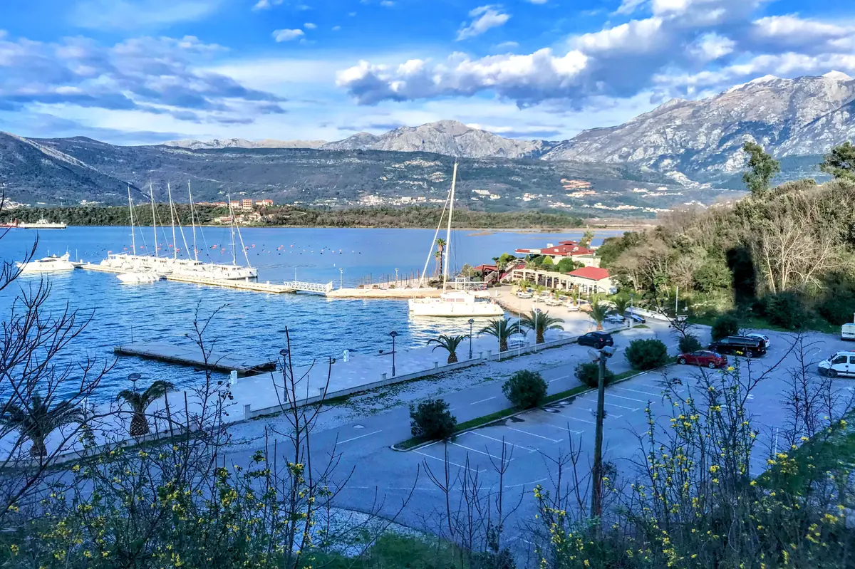 Aerial view of Solila Beach (Movida Beach) Tivat featuring palm trees and sailboats docked in the adjacent marina