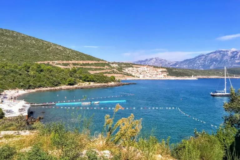 White luxury sunbeds and umbrellas at Almara Beach Club in Oblatno Bay, featuring a clear turquoise sea and a sophisticated Mediterranean lounge atmosphere.