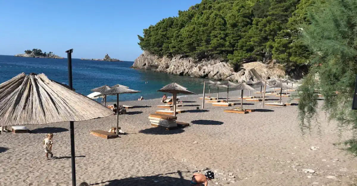 View of Lučice Beach cove surrounded by pine trees and turquoise water with Katic and Sveti Nedelja Islands in the background, near Petrovac, Montenegro
