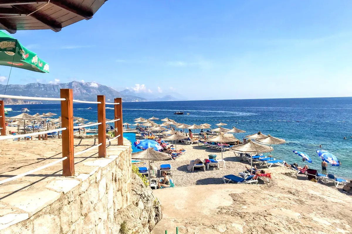 vView of Ploče Beach near Budva, showing the multi-level stone terraces and crystal-clear turquoise Adriatic water against a rugged rocky coastline