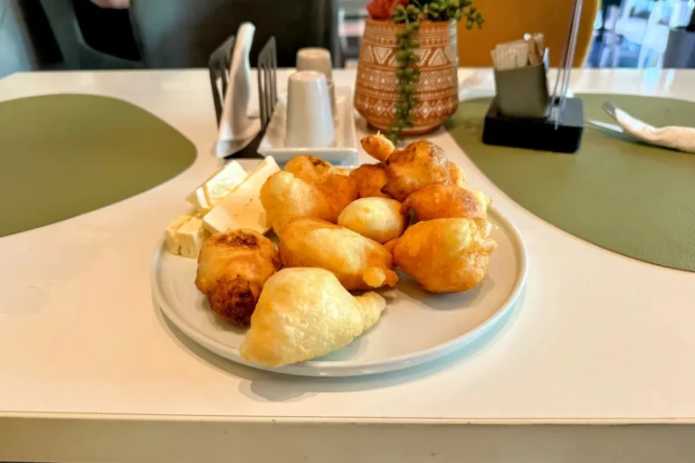 A plate of fresh, golden-brown Montenegrin priganice served with honey and cheese, a traditional Balkan breakfast delicacy.