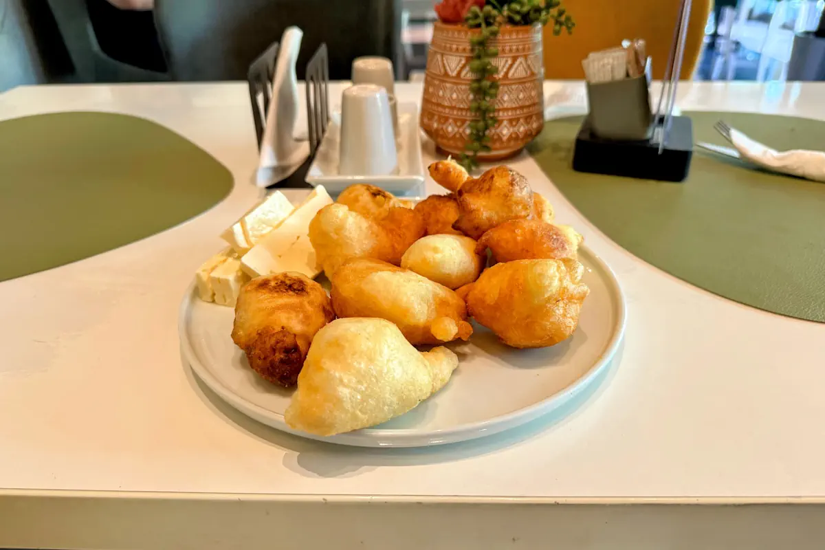 A plate of fresh, golden-brown Montenegrin priganice served with honey and cheese, a traditional Balkan breakfast delicacy.