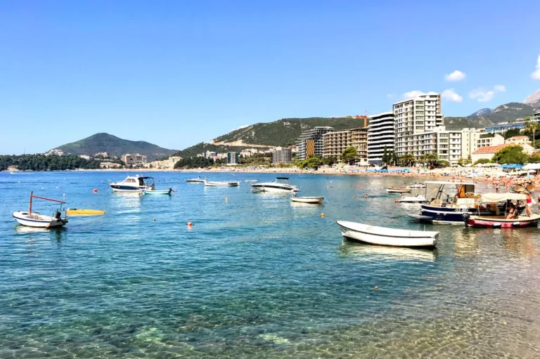 Becici Beach photo taken from the Rafailovici neighborhood, overlooking fishing boats, upscale hotels, red pebbles, and gin-clear waters