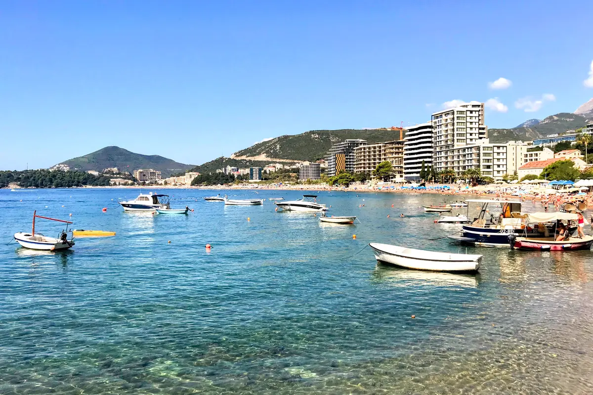 Becici Beach photo taken from the Rafailovici neighborhood, overlooking fishing boats, upscale hotels, red pebbles, and gin-clear waters