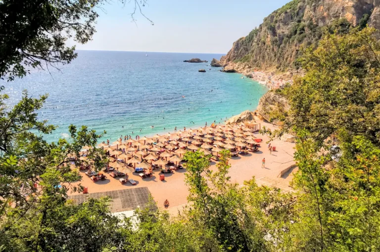 Aerial view of Perazica Do beach near Petrovac Montenegro showing turquoise water, white pebbles, and the sandstone cliffs of the Budva Riviera.