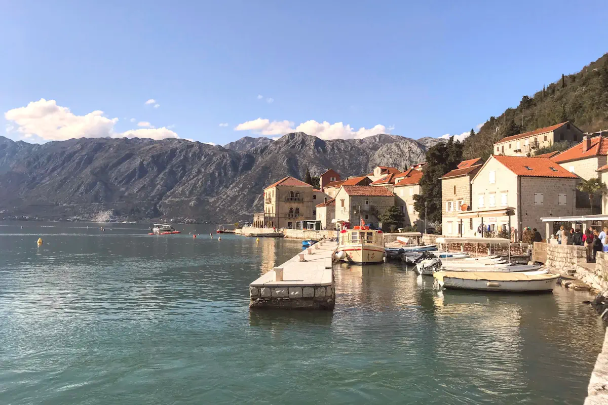Waterfront dining terraces in Perast with a view of Our Lady of the Rocks and the Bay of Kotor, Montenegro.