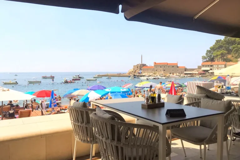 An al fresco table at a beachfront terrace, showing the best restaurants in Petrovac with a view of the Kastelo and the marina.