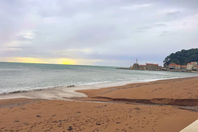 A moody, peaceful view of Petrovac beach and the stone marina pier in the off-season, showing the coastal charm of the Budva Riviera.