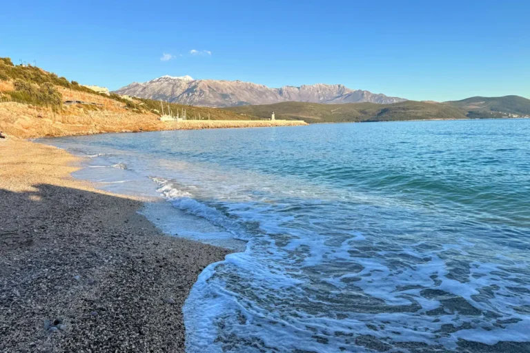 The turquoise waters and manicured shoreline of Marina Beach at Luštica Bay, featuring the luxury promenade and stone architecture in the background.