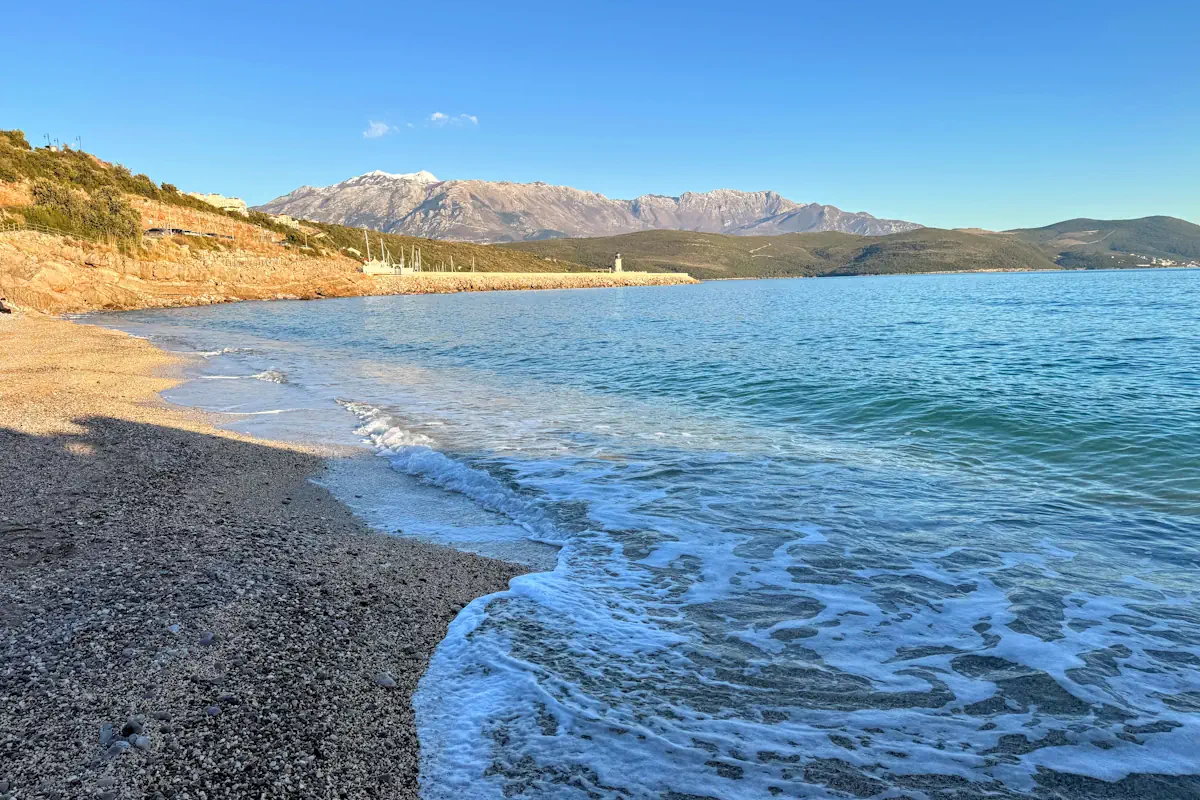 The turquoise waters and manicured shoreline of Marina Beach at Luštica Bay, featuring the luxury promenade and stone architecture in the background.